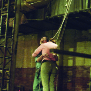 Kaz and Helen stand bound in an embrace by dangling ropes